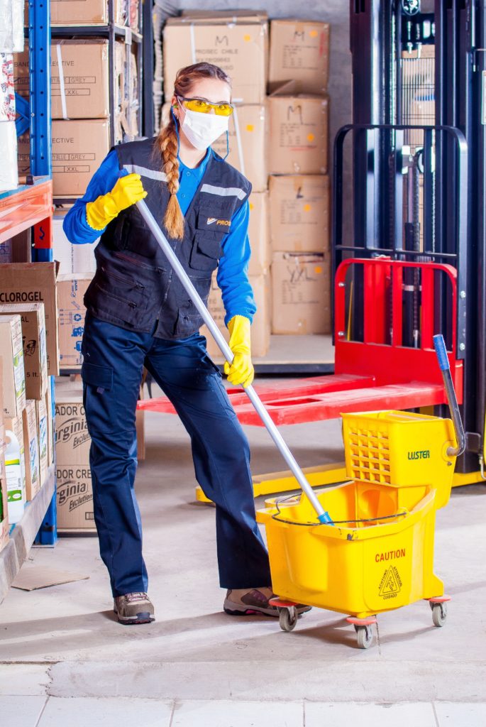 Woman in mask and gloves mopping floor.