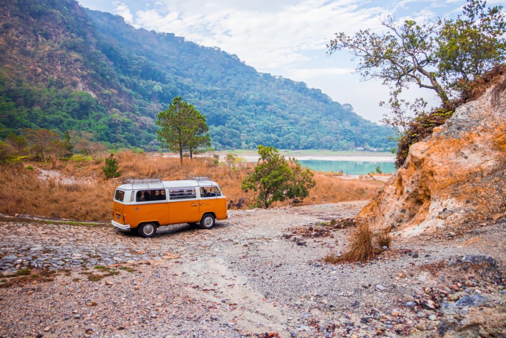 Volkswagen bus parked on unpaved trail near lake.