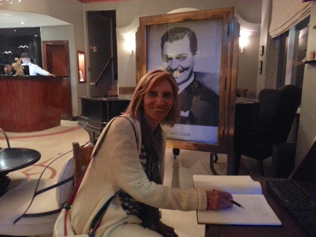 woman poses in front of Clark Gable picture at Cadet Hotel Lobby, Miami Beach.