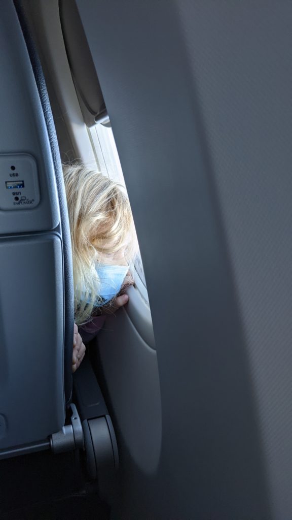 Young girl looking out the window of an airplane with face mask.