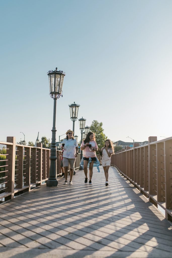 Two women and girl walk across a pedestrian bridge carrying beverages