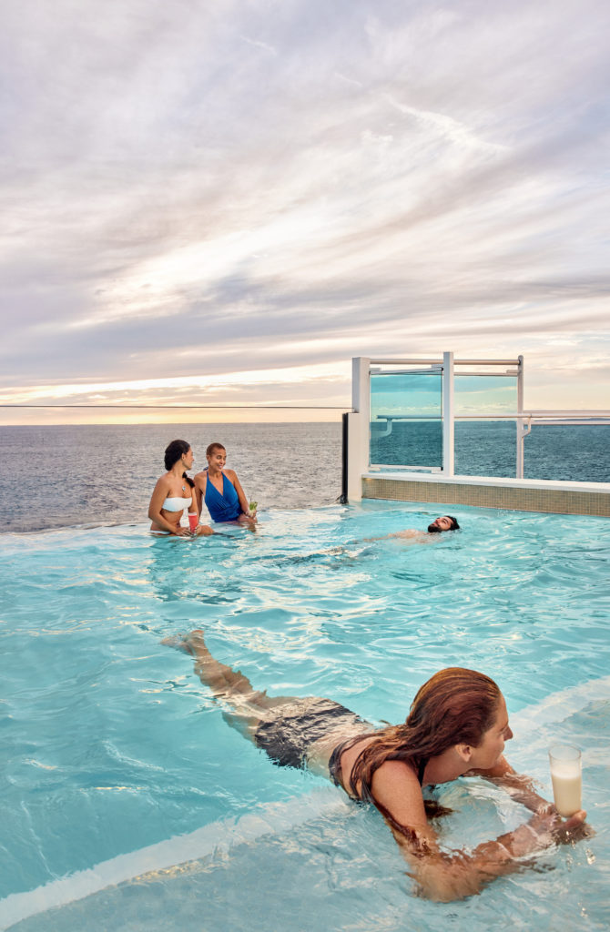 Women with drinks relaxing in the pool on the deck of the Enchanted Princess as a man swims.