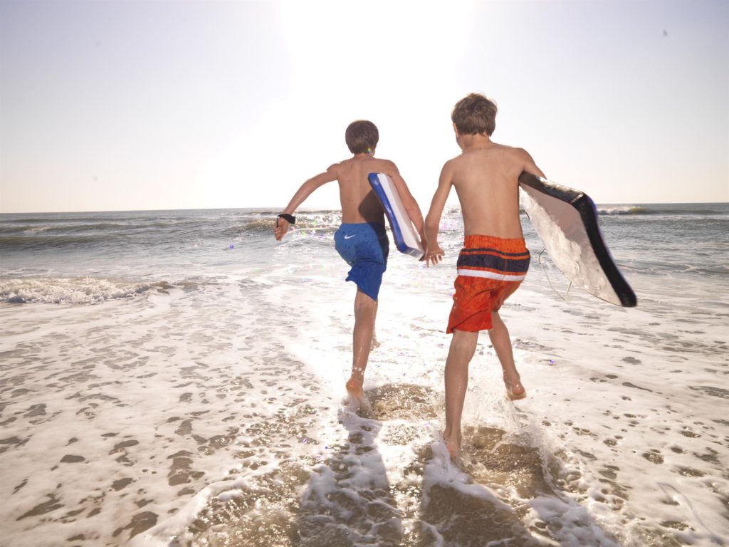 Two boys run into surf carrying boogie boards. Photo c. BaldHeadIsland.com