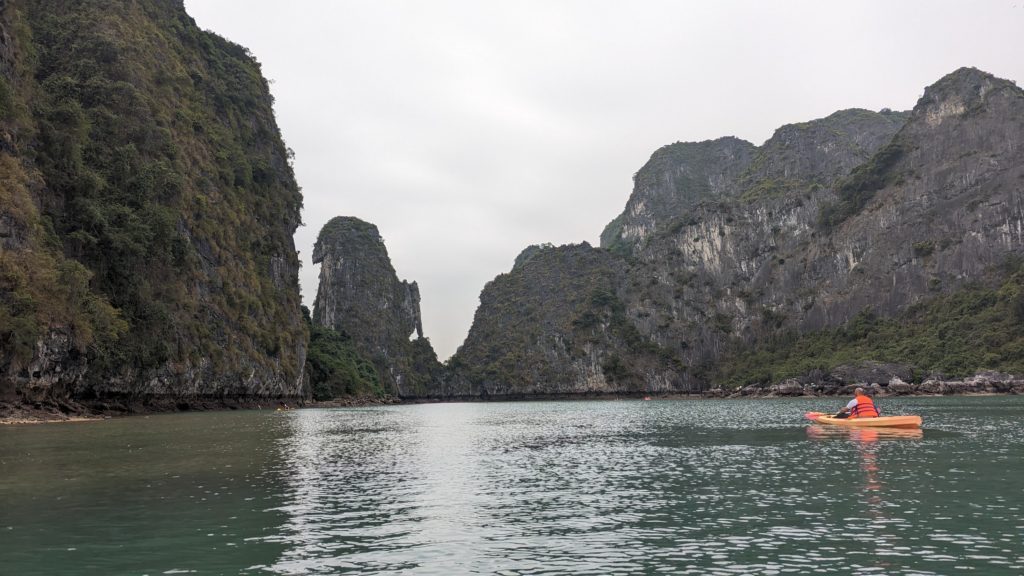 Single kayaker paddles up to karst formations in Halong Bay, Vietnam.