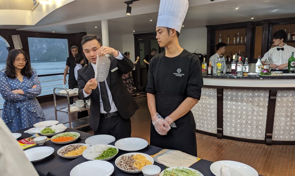 Ambassador cruise staff and chef teach a spring roll making class aboard ship.