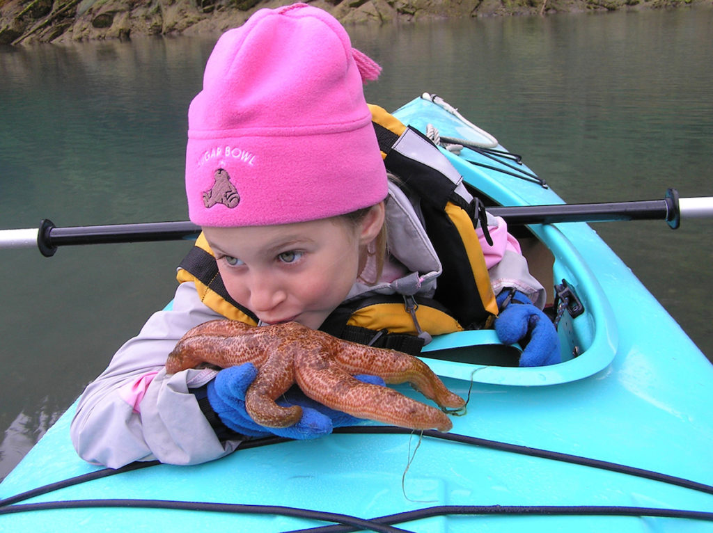 Young girl examines a starfish up close on a kayak excursion with Uncruise Adventures in Alaska.