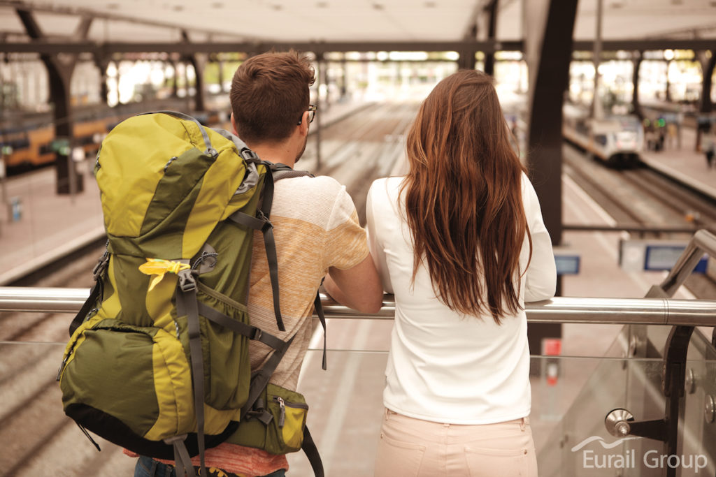 Young couple watching trains pull in at a large railway station.