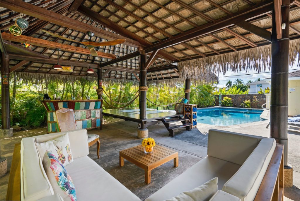 Tropical style hotel lobby with white lounge chairs and pool in background.