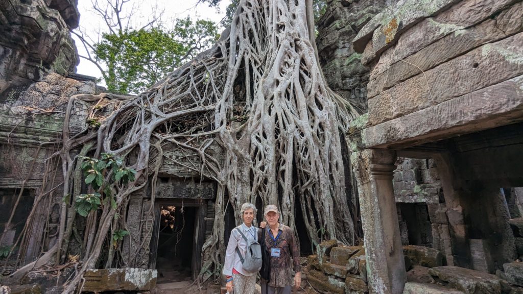 Couple pose in front of ancient Banyan tree at the Ta Prohm temple seen in