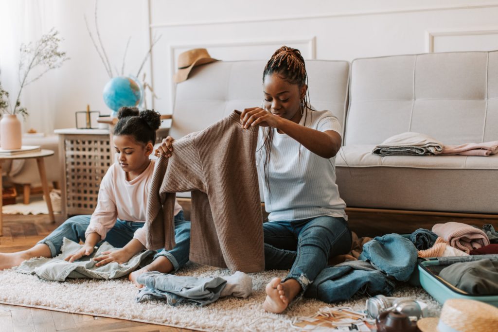 Mother and daughter sit on the floor and fold clothes to put into a suitcase.