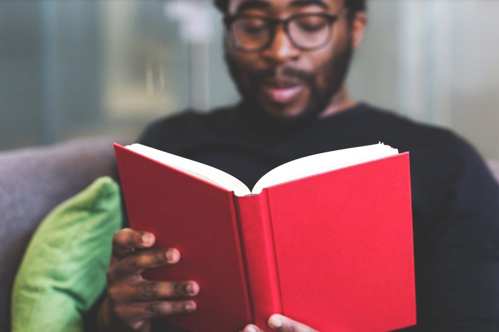 Man reading a book with a red cover.