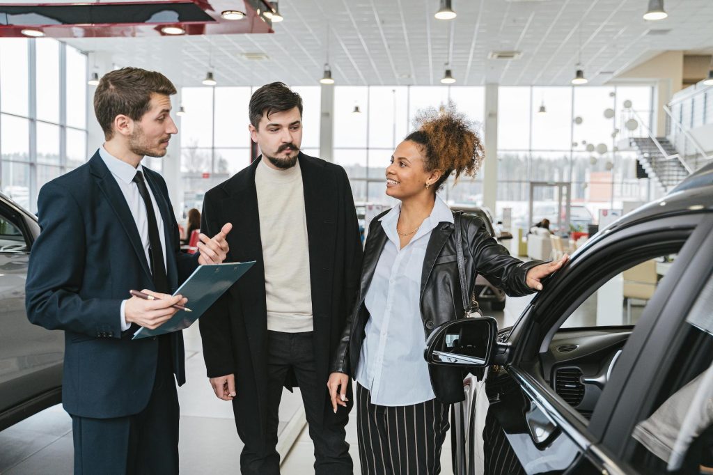 Couple with car dealer to buy a used fuel efficient car. Photo by Shkrabaanthony for pexels.