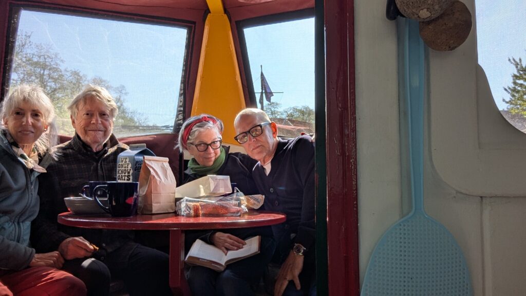 Four older people enjoy breakfast and coffee in the bow of the Otisco, a rental barge houseboat from Erie Canal Adventures.