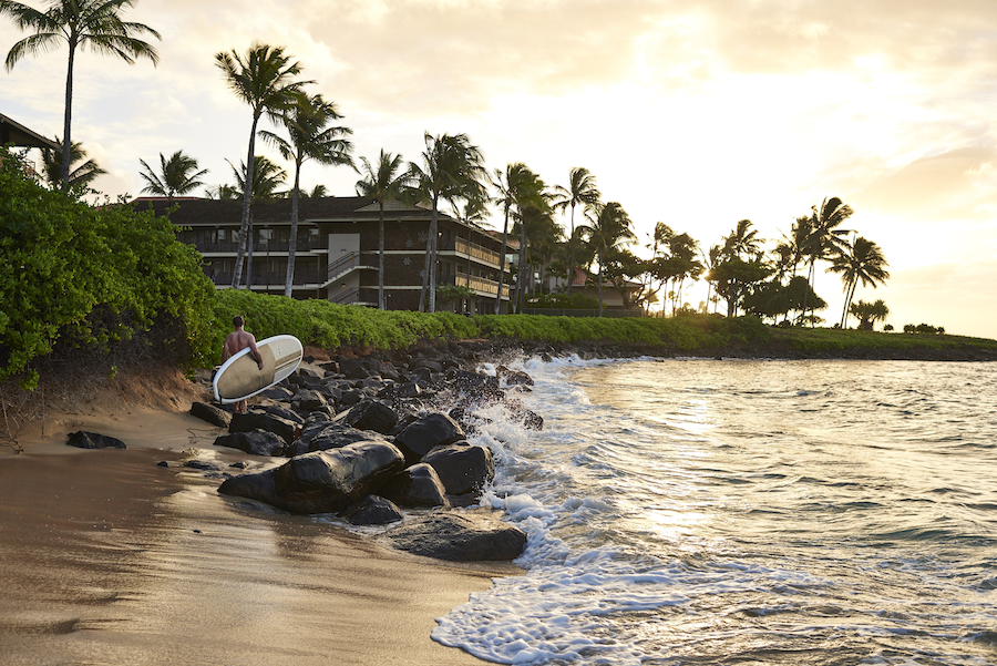 Surfer carrying a surfboard heads back to the Ko’a Kea Resort on the Hawaiian island of Kauai. Photo c. Ko’a Kea Resort Po’ipu Beach
