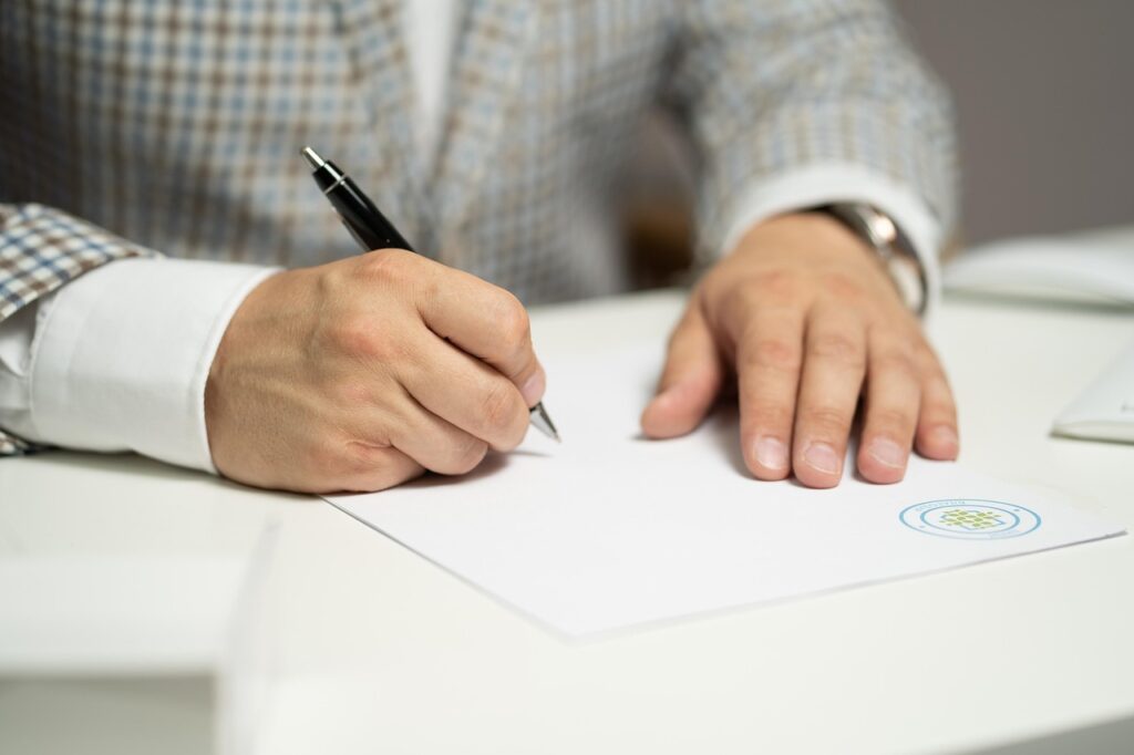 Man fills out a form and signs it with a pen. Photo c. Maximilianovich for pixabay.