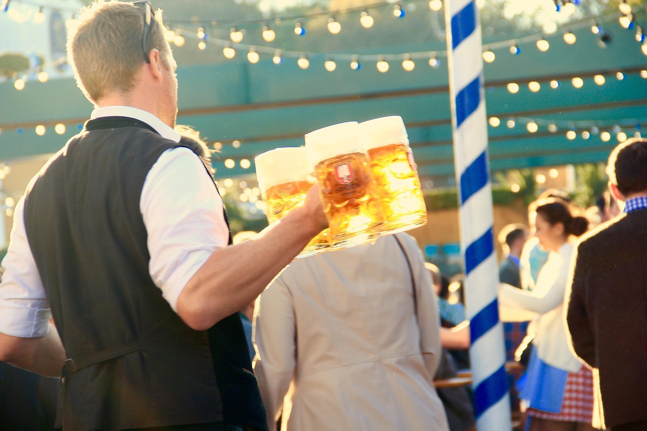 Waiter carrying three beer steins through Oktoberfest crows. Photo by Motointermedia c. pixabay.
