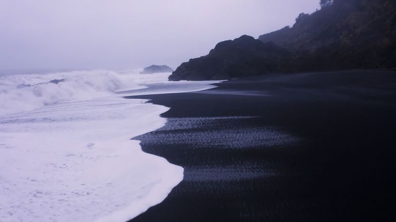 The Contrast Between Black Sand And White Foam Is Visually Unsettling