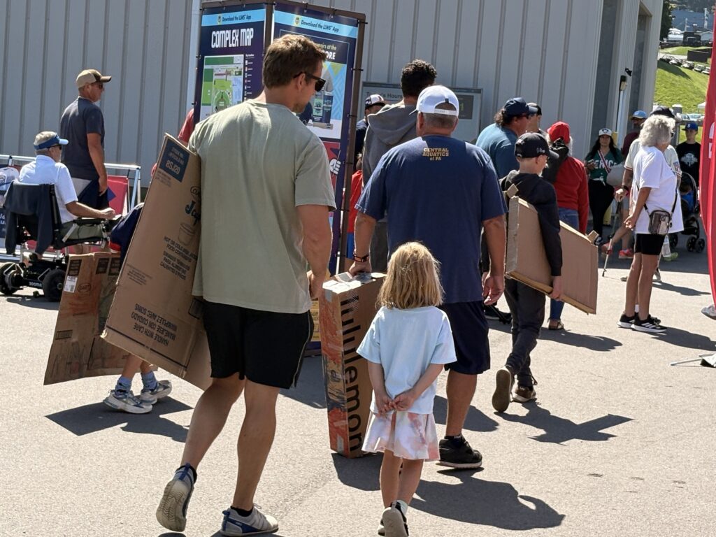 Families carry in cardboard 'sleds' for sliding down the hill behind Lamade Stadium during the Little League World Series.