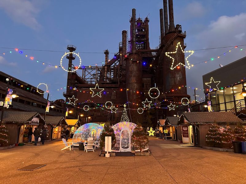 A Holiday Market Glowing Beneath Giant Steel Stacks